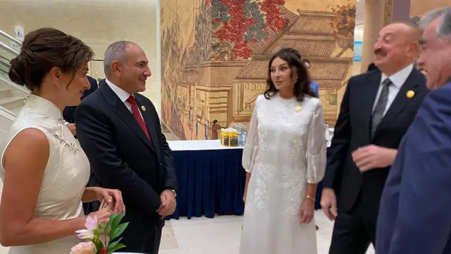 Şəklin sol tərəfində ağ geyimdə olan Anna Hakobyan görünür. Onun yanında Ermənistan Baş naziri Nikol Paşinyan dayanıb. Paşinyan gülümsəyir. Ondan sağda ağ geyimdə olan Mehriban Əliyeva dayanıb. Onun sağında isə İlham Əliyev dayanıb və o, gülür.
Copyright 