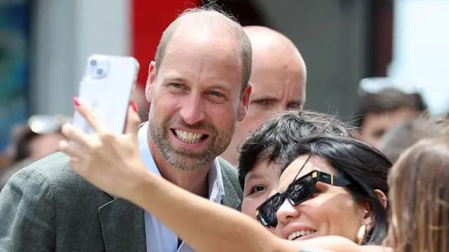 Şahzadə William günəş eynəyi taxmış bir qadın və uşaqla selfie çəkdirir