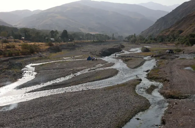 İranlılar daşlı bir çay yatağında xalça sərərək piknik edirlər; çayda isə sadəcə bir neçə nazik su axını qalıb.